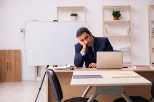 man in suit, sitting at a desk with his head propped on his hand looking tired and frustrated